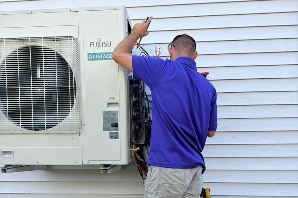 Technician servicing outdoor air conditioning unit on house exterior wall.