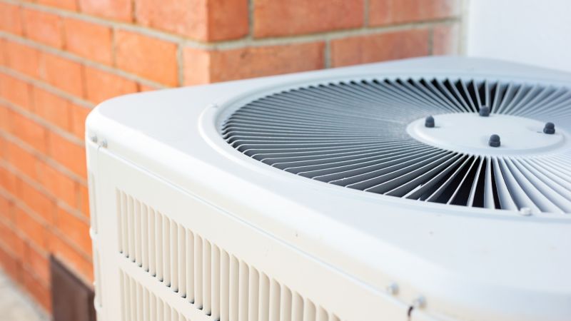 Outdoor air conditioning unit near red brick wall for home cooling.