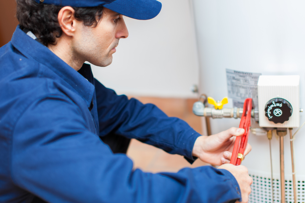 Technician in blue uniform fixing a water heater with a wrench in a home setting.