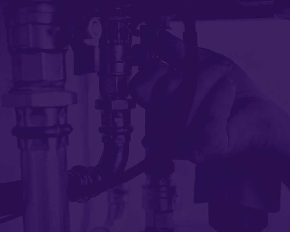 Hands tighten a valve on a metal pipe in an industrial plumbing setup, close-up view