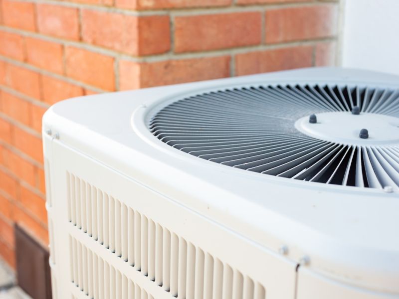Outdoor air conditioning unit near red brick wall for home cooling.