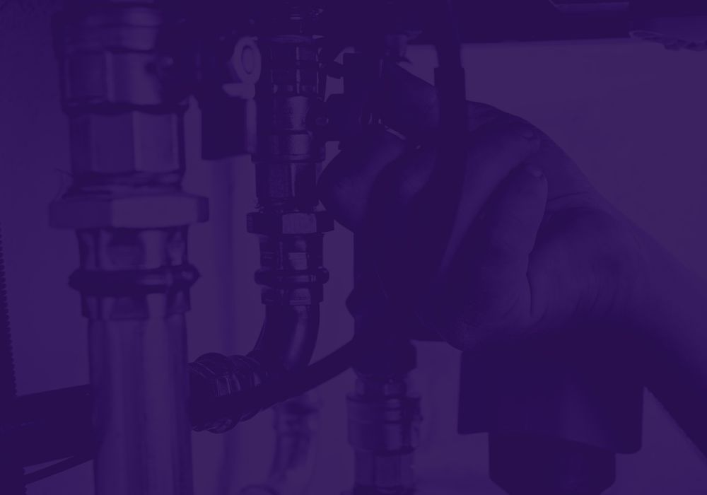 Hands tighten a valve on a metal pipe in an industrial plumbing setup, close-up view