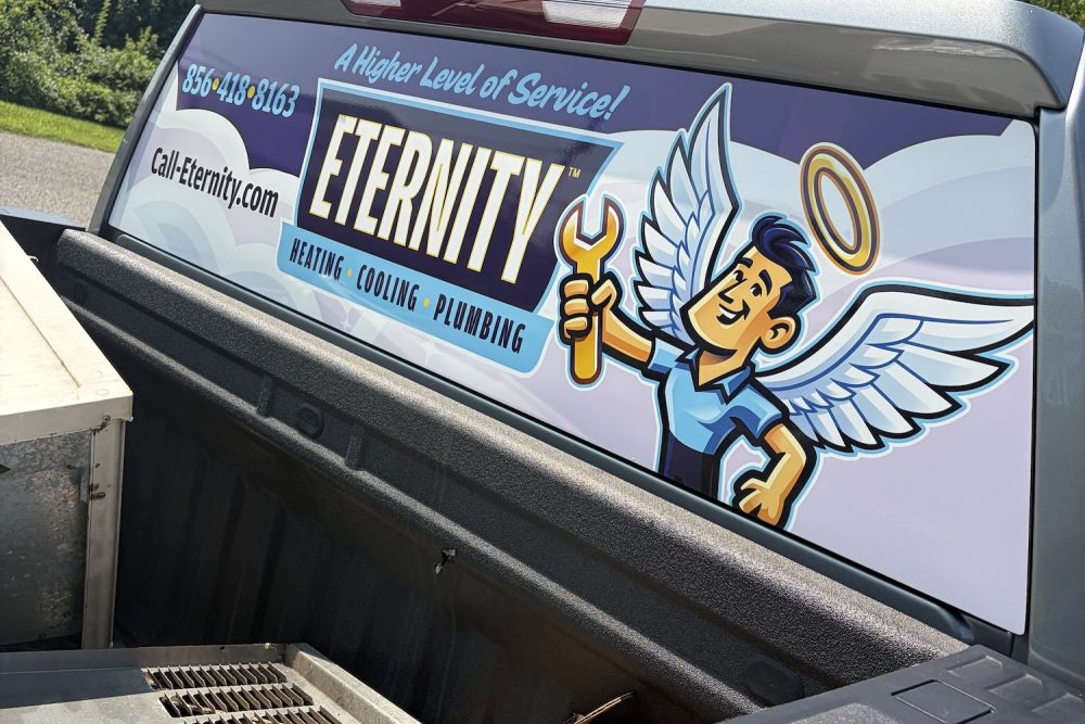 Truck tailgate with Eternity Heating, Cooling, Plumbing ad featuring angel with wrench. Contact and website info displayed.